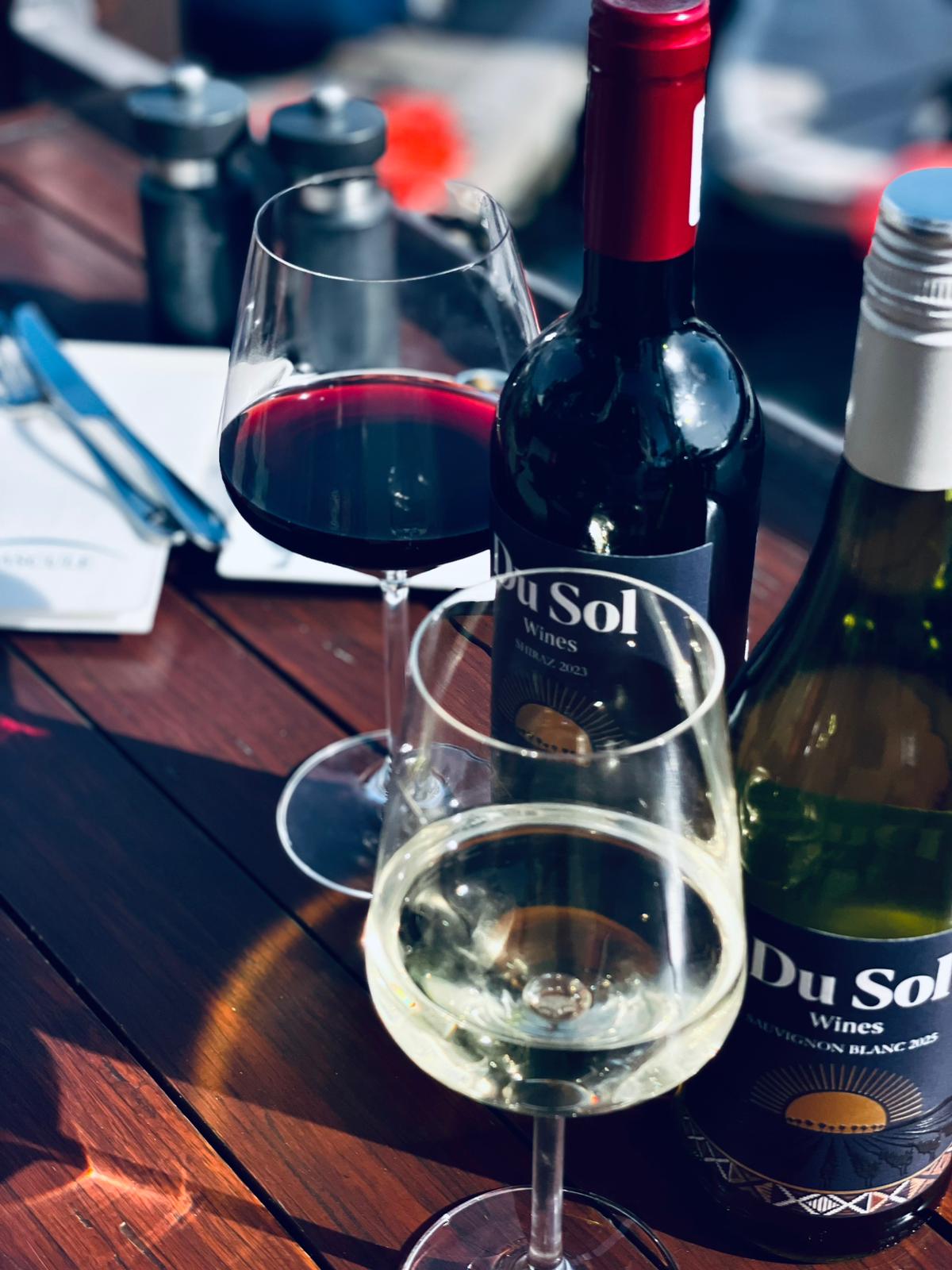 Glasses of Du Sol red and white beside the bottles on a wooden table
