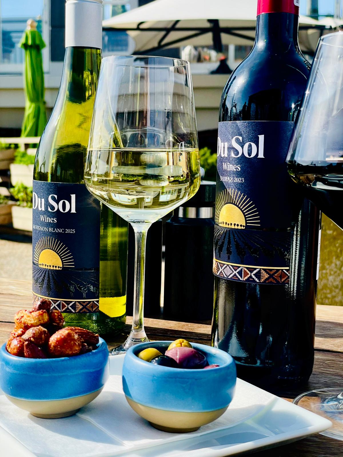 Sauvignon Blanc and Shiraz bottles with a glass of white and tapas outdoors