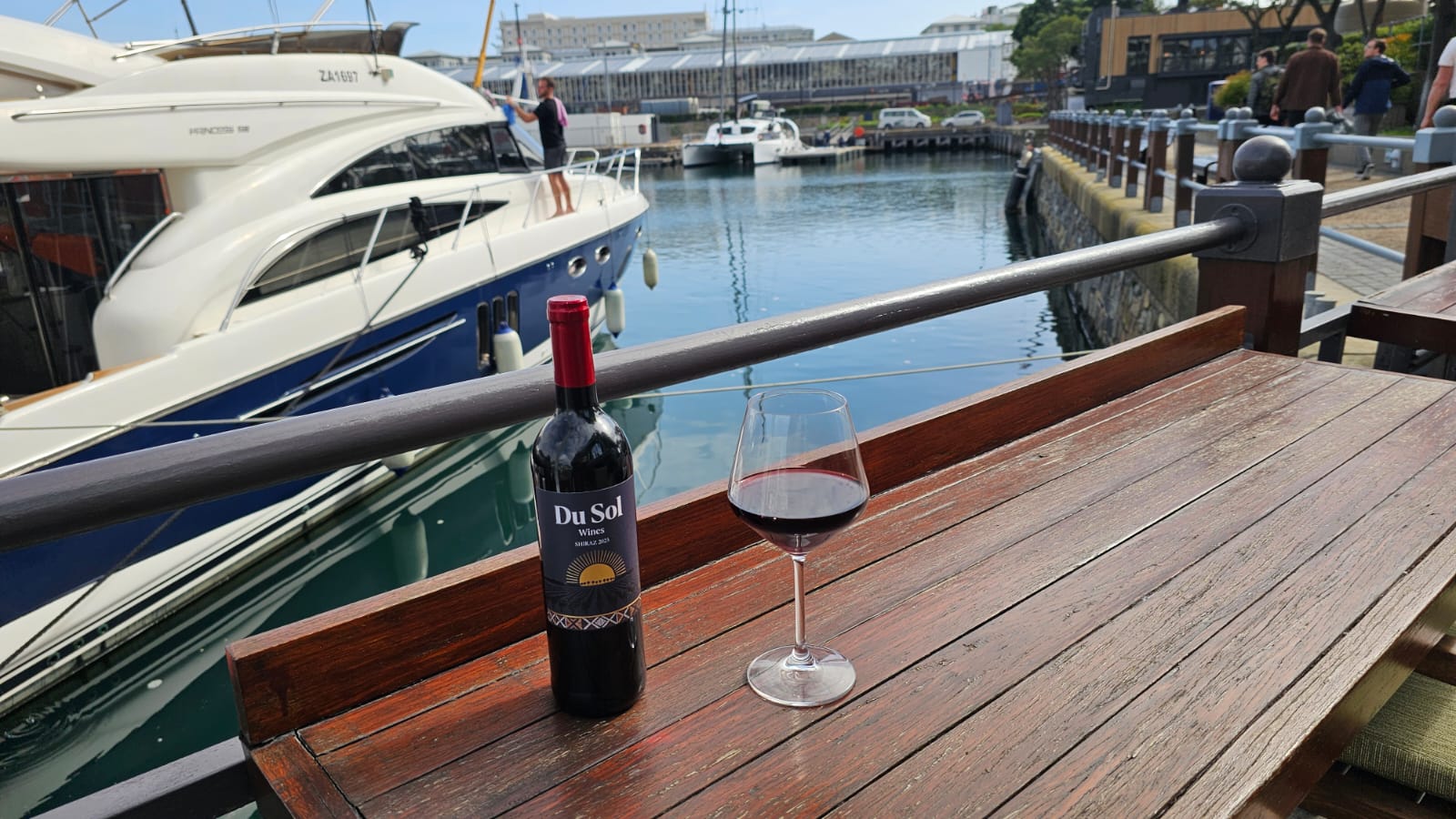 A bottle and glass of Du Sol Shiraz at the marina with yachts behind