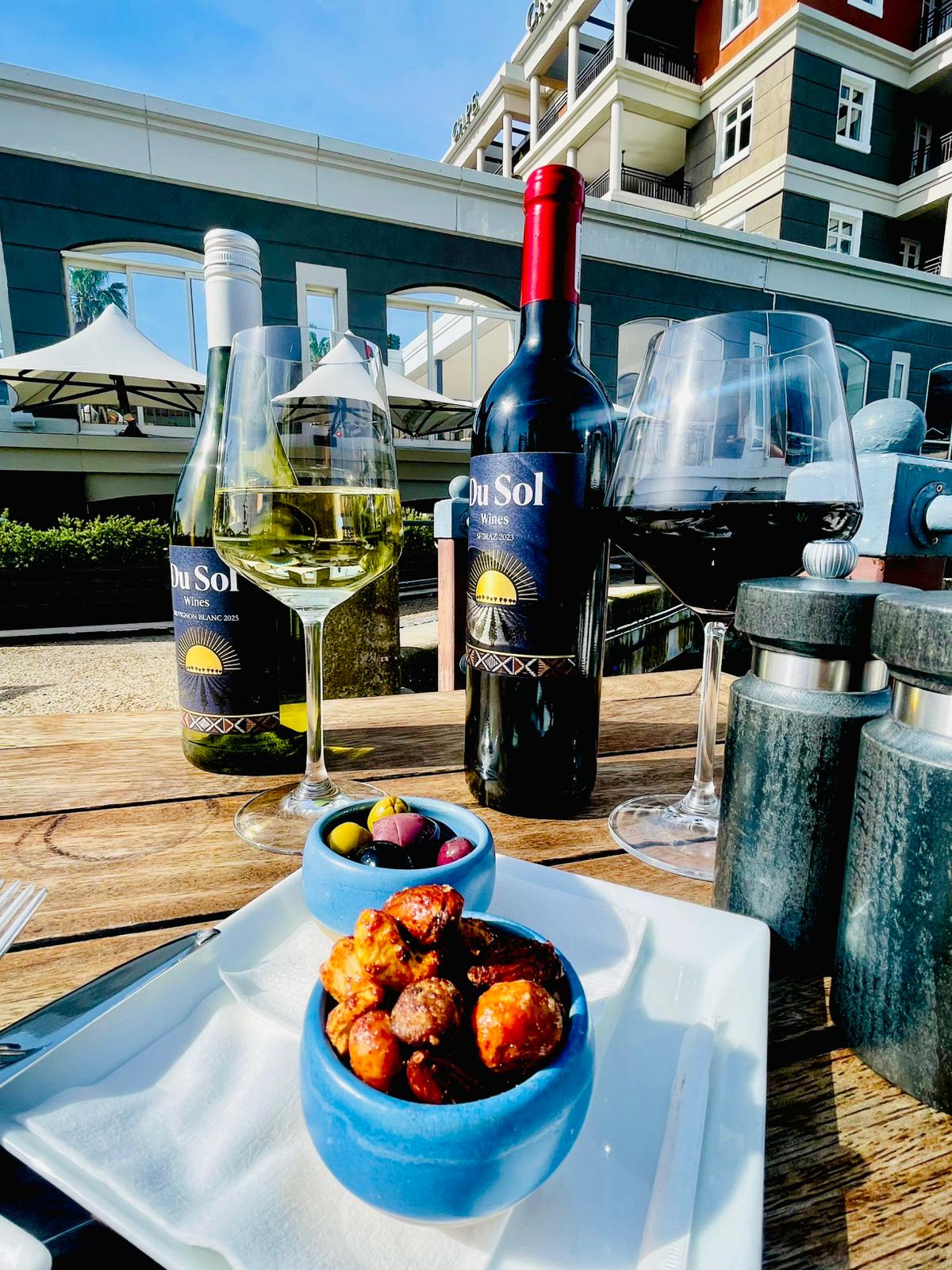 Du Sol Sauvignon Blanc and Shiraz with glasses and snacks at a waterfront café