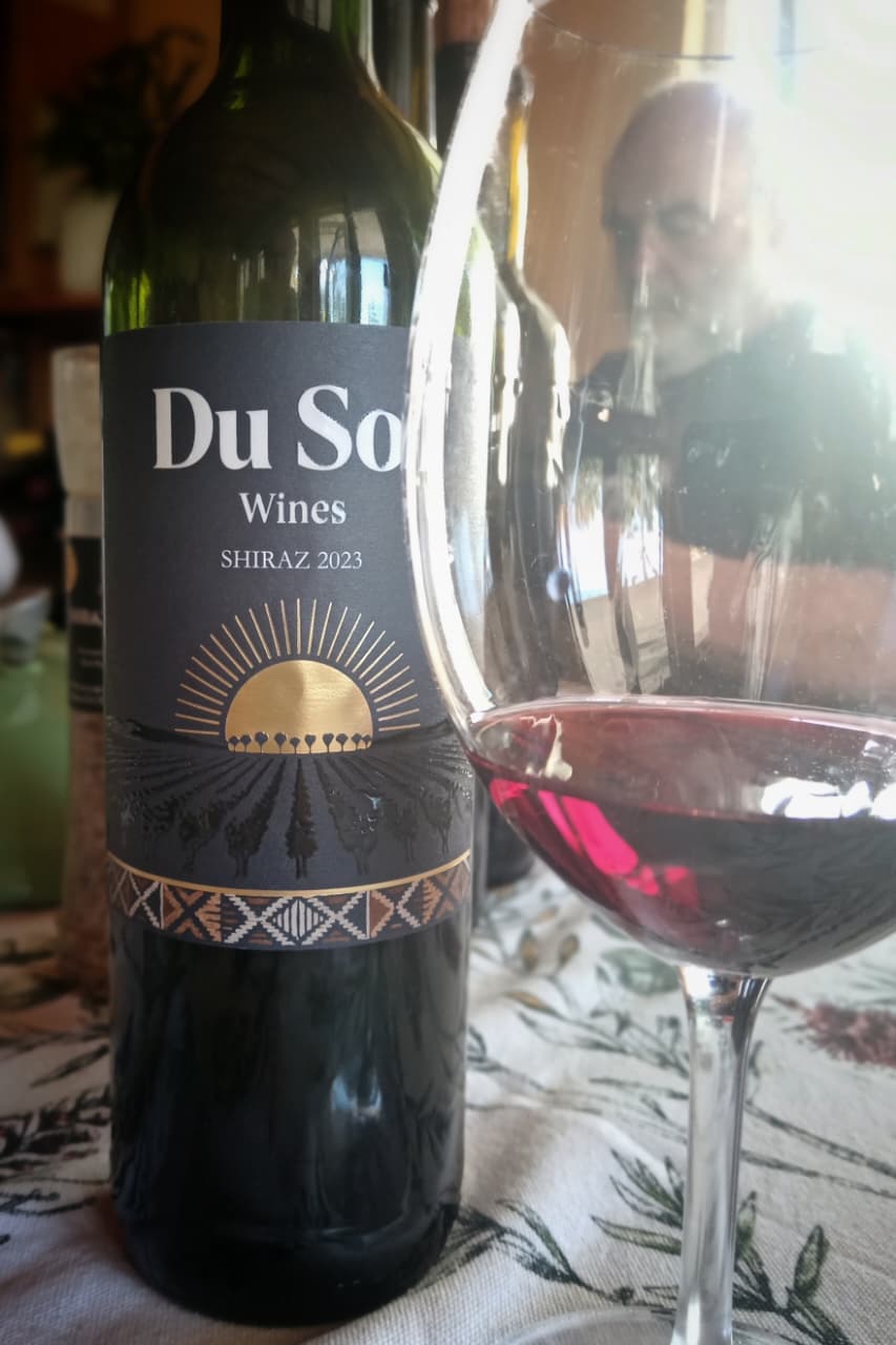 A bottle of Du Sol Shiraz 2023 beside a glass of red wine at the table